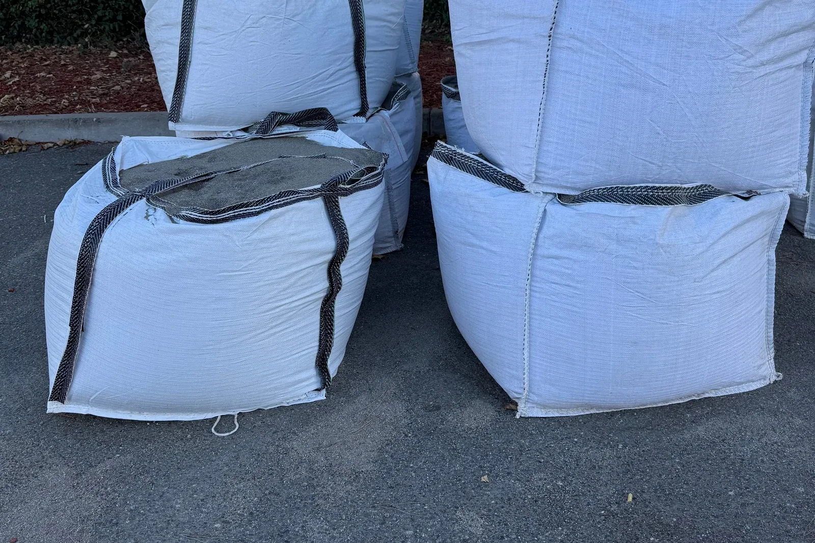 Filled white bulk bags stacked two high on a paved outdoor staging yard