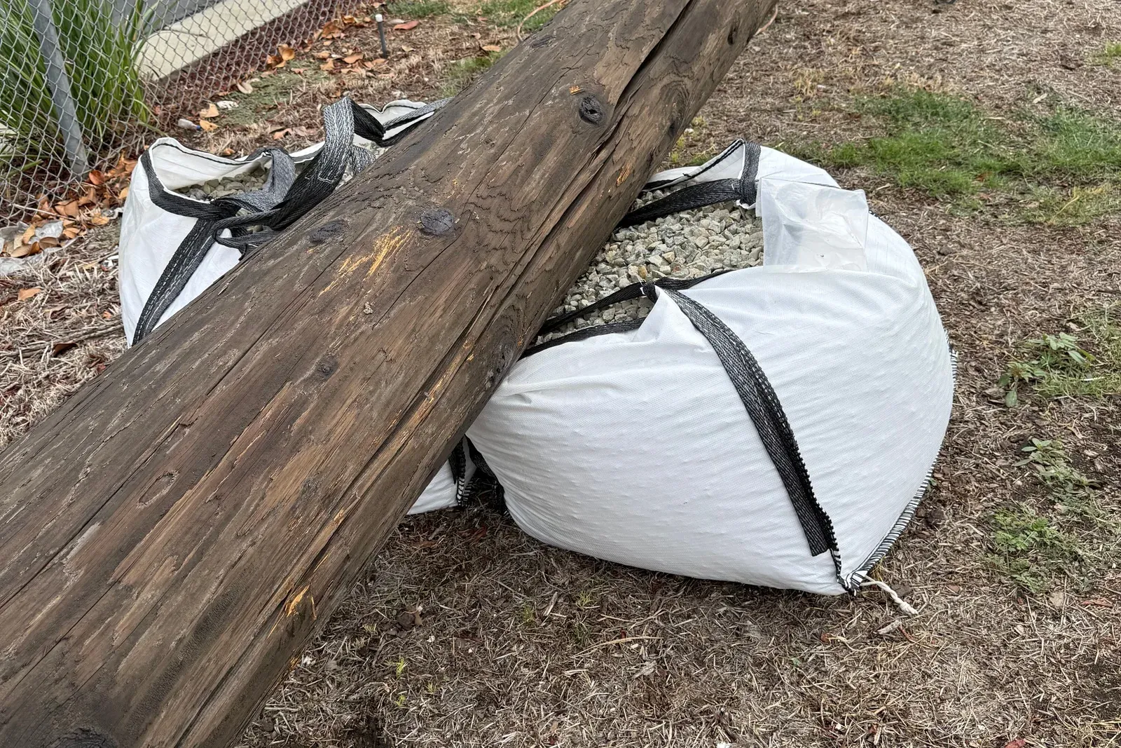 Gravel-filled bulk bag with a timber utility pole resting across it on open ground