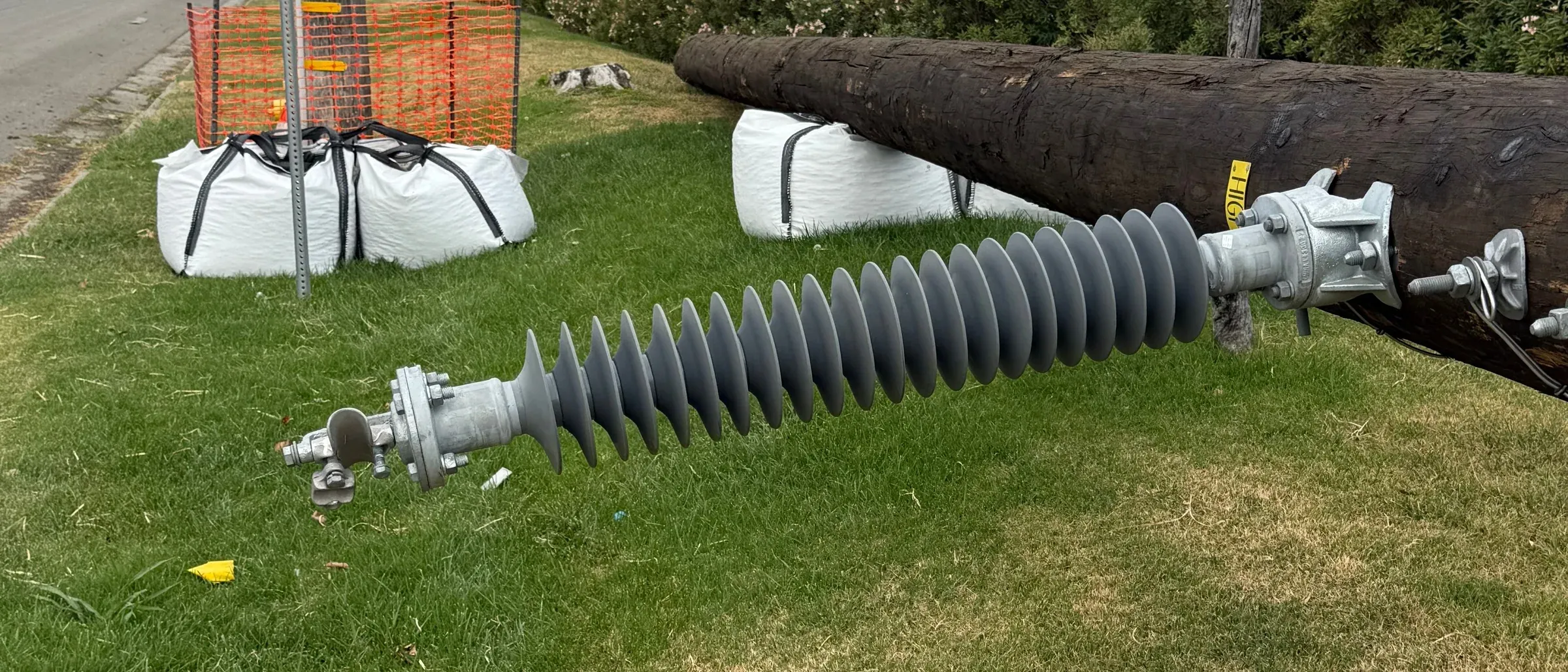 Filled bulk bags cribbing a timber utility pole laid on a roadside verge beside its insulator during a pole replacement