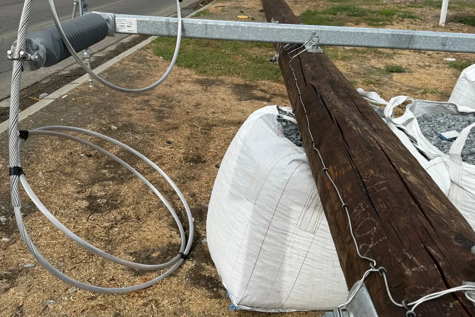 Rock-filled bulk bags and coiled guy wire at a roadside utility pole installation