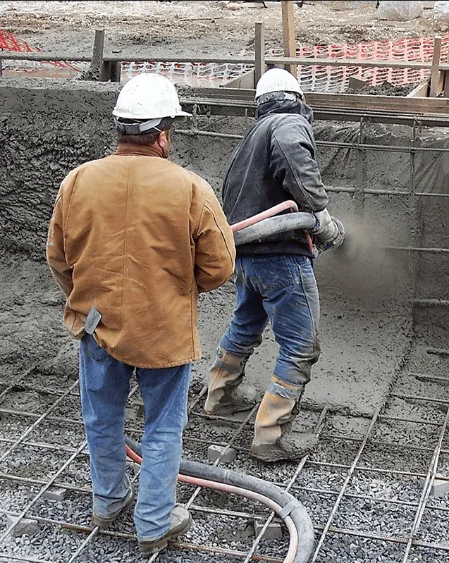 Construction crew in hard hats spraying shotcrete over a steel rebar mat